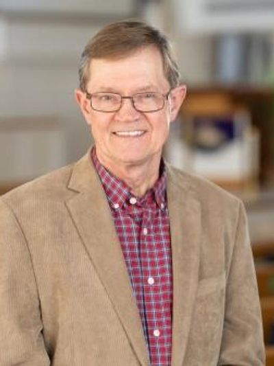 Older man in glasses and beige blazer smiling at the camera.