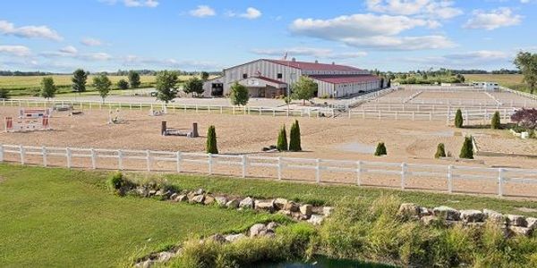 A spacious equestrian facility with riding arenas and a large barn under a blue sky.