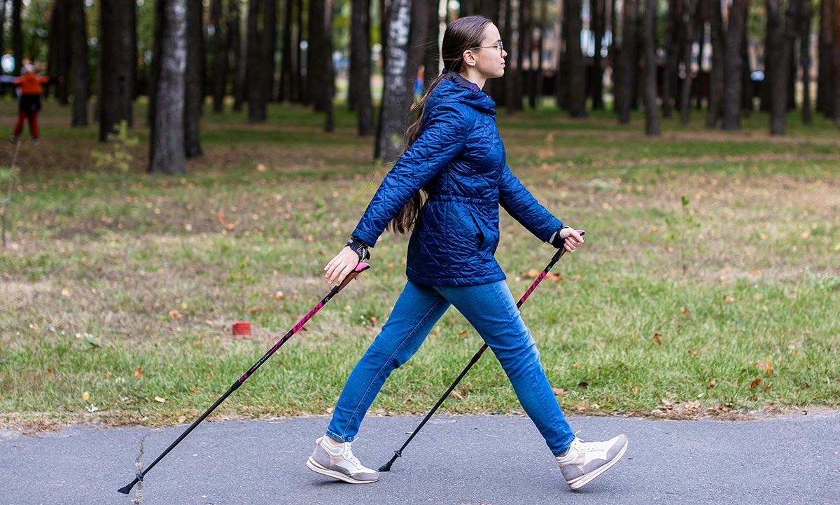 A woman in a blue jacket walking with Nordic Walking poles in a park.