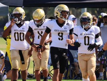 Four high school football players from North Manatee in uniform walking on the field.