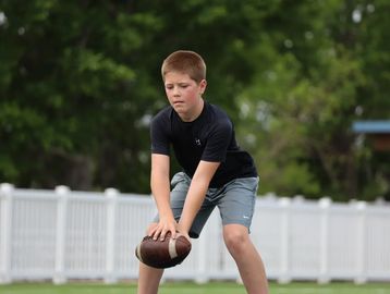 A boy practices holding a football outdoors on a grassy field.