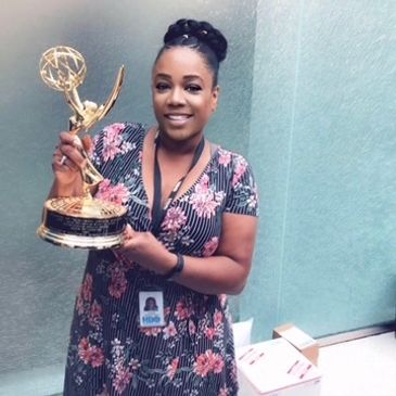 Woman proudly holding an Emmy Award with a smile.