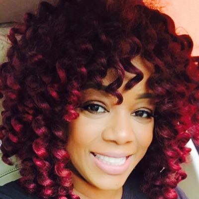 Smiling woman with vibrant curly hair and bright eyes.
