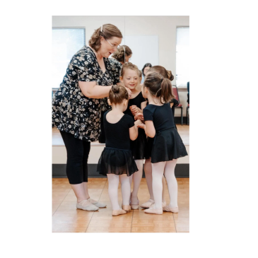 Ballet instructor guiding young girls in black leotards during dance class.