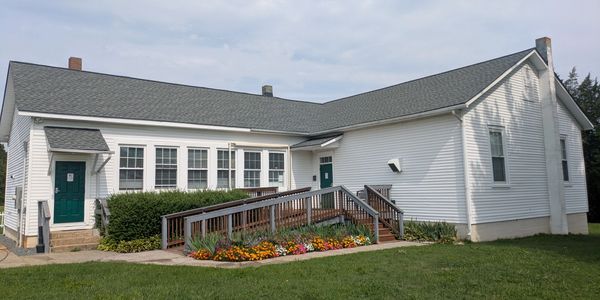 White single-story building with green doors and a wooden ramp.
