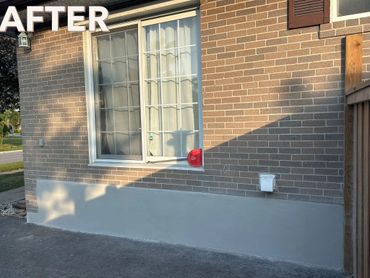 Brick wall with freshly repaired and painted lower section under a window.