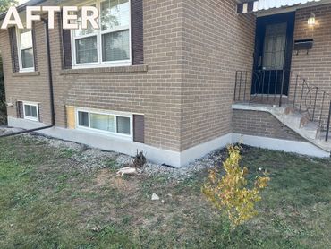 Freshly repaired and painted foundation of a brick house with a small tree in front.