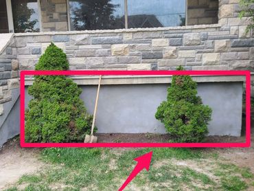 A house exterior with a parged wall and brick wall behind it, flanked by green shrubs.