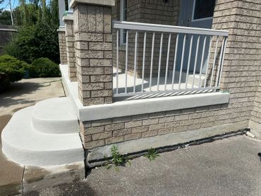 Freshly painted concrete steps and porch with a white railing on a brick house.