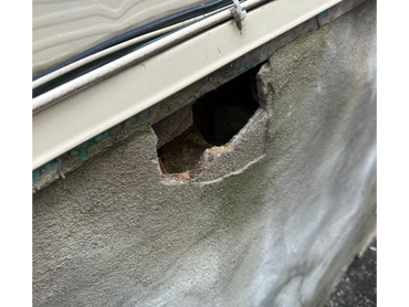 Damaged exterior wall with a hole and visible wear.