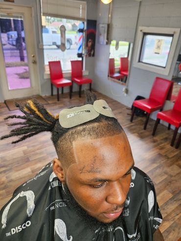 Man with styled black dreadlocks and a beard in a barbershop.