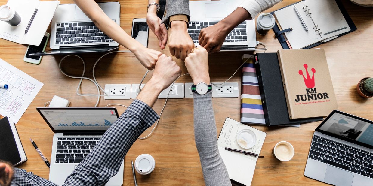 A team fist bumping, with their laptops, ready for new projects.