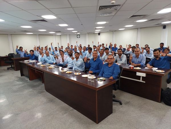 Group of men in a meeting room raising their hands and smiling.