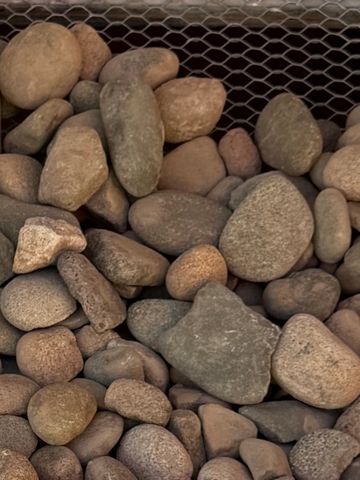 A collection of smooth river rocks piled together with a metal mesh in the background.