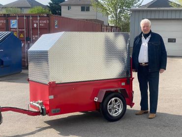 Man standing beside a red and silver trailer.