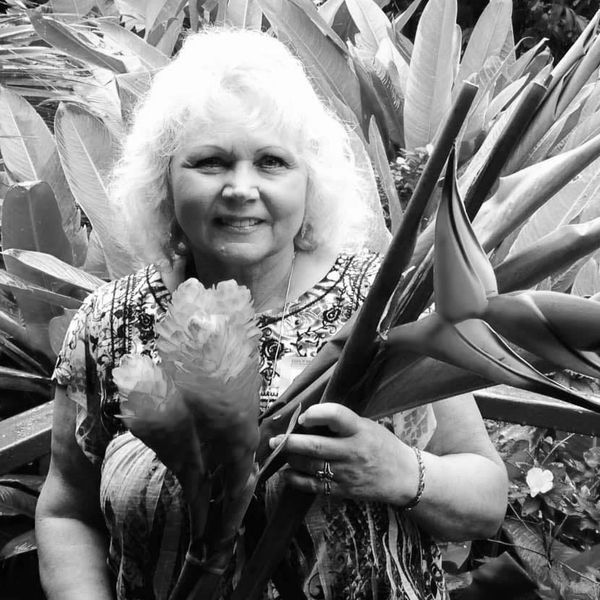 Smiling woman holding tropical flowers in a lush garden.