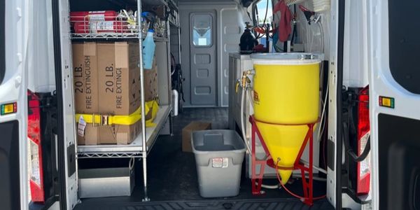 Open van loaded with fire extinguishers, equipment, and a large yellow container.