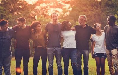 Group of friends standing arm in arm outdoors at sunset.