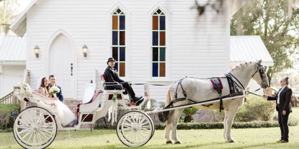 Bride and groom in horse-drawn carriage in front of white chapel.