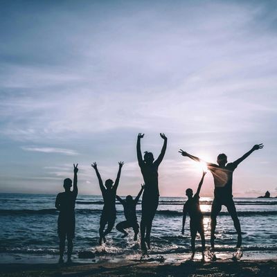 Silhouettes of six people jumping joyfully on the beach at sunset.