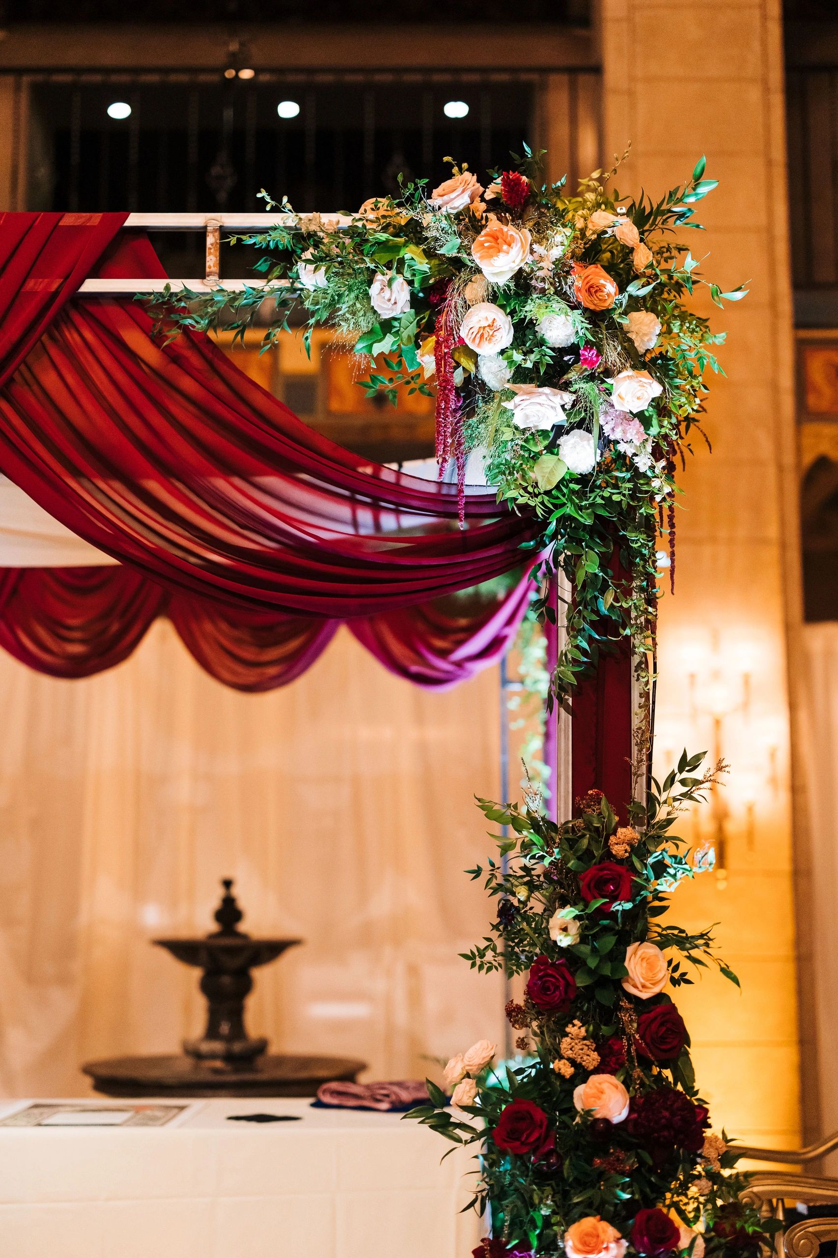 Elegant floral wedding arch with burgundy drapes and mixed roses.