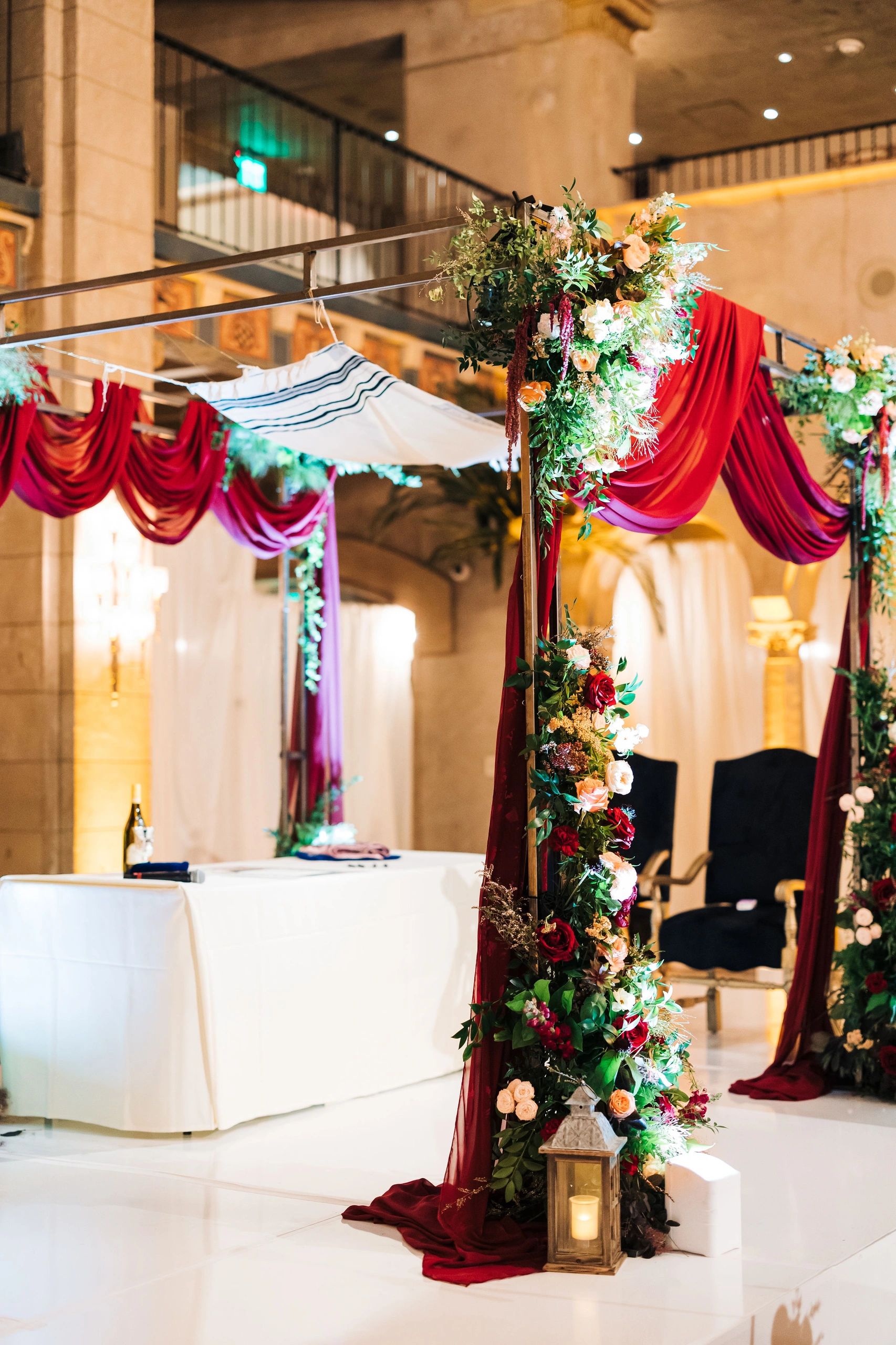 Elegant wedding chuppah decorated with flowers and burgundy drapes in a luxurious venue.