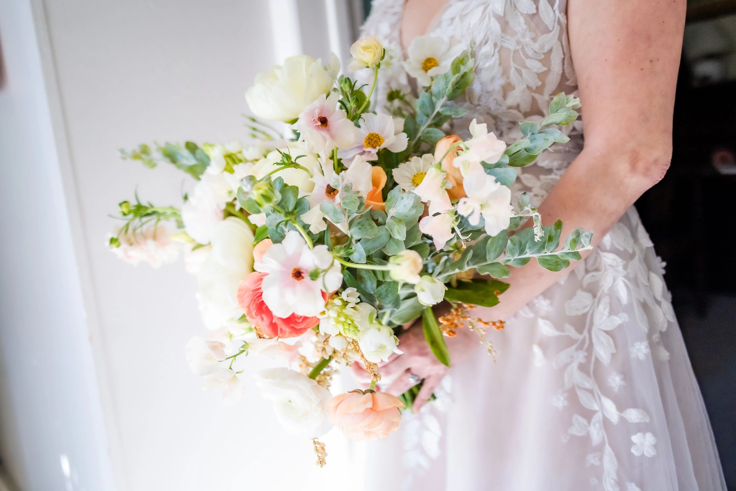Bride holding a vibrant bouquet with white, peach, and pink flowers.