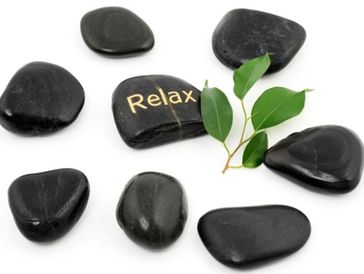 Black stones arranged with one stone engraved 'Relax' and green leaves.