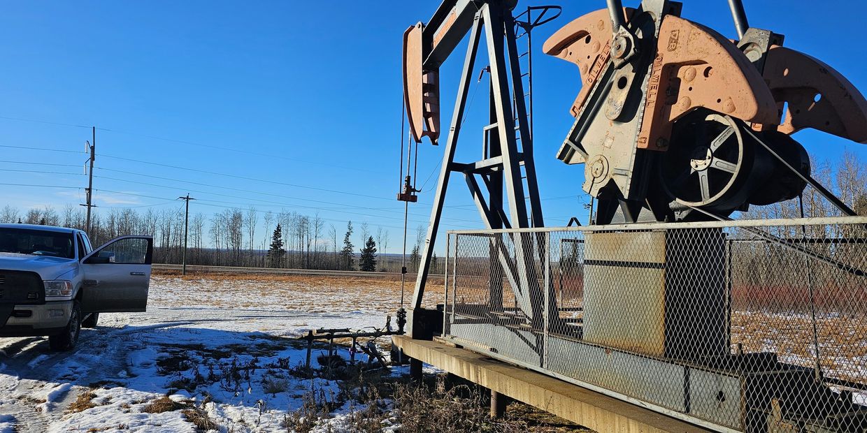 Oil pumpjack in a snowy field on a clear day with a truck nearby.