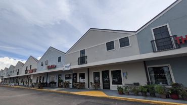 Row of modern commercial buildings with shops and restaurants under a cloudy sky.