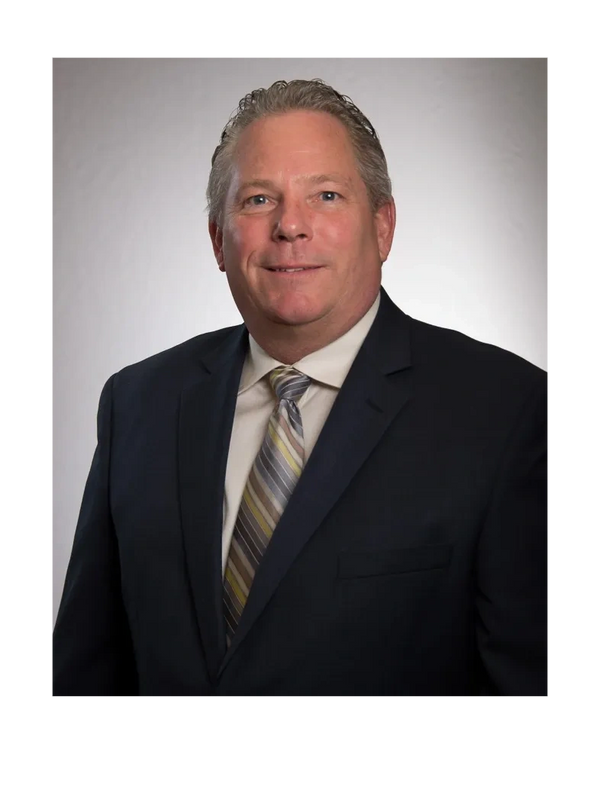 Professional man in a dark suit and striped tie smiling against a plain background.