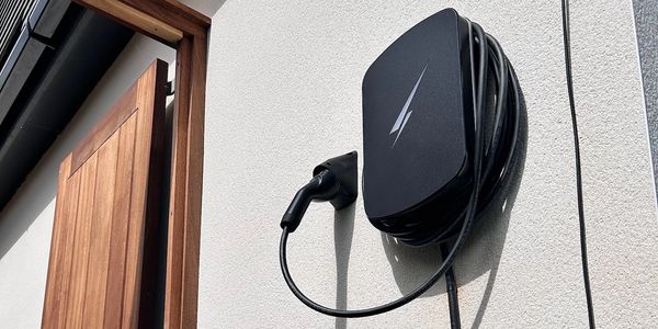 Electric vehicle charging station mounted on a white house wall next to a wooden door.