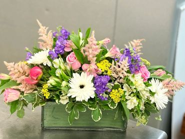 White vase floral arrangement with roses, lilies, and stock flowers.