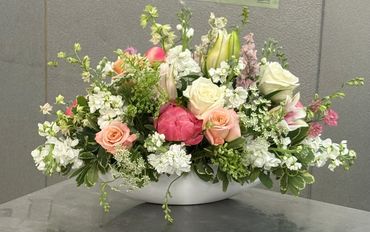 Elegant floral centerpiece with roses, lilies, and stock in a white vase.