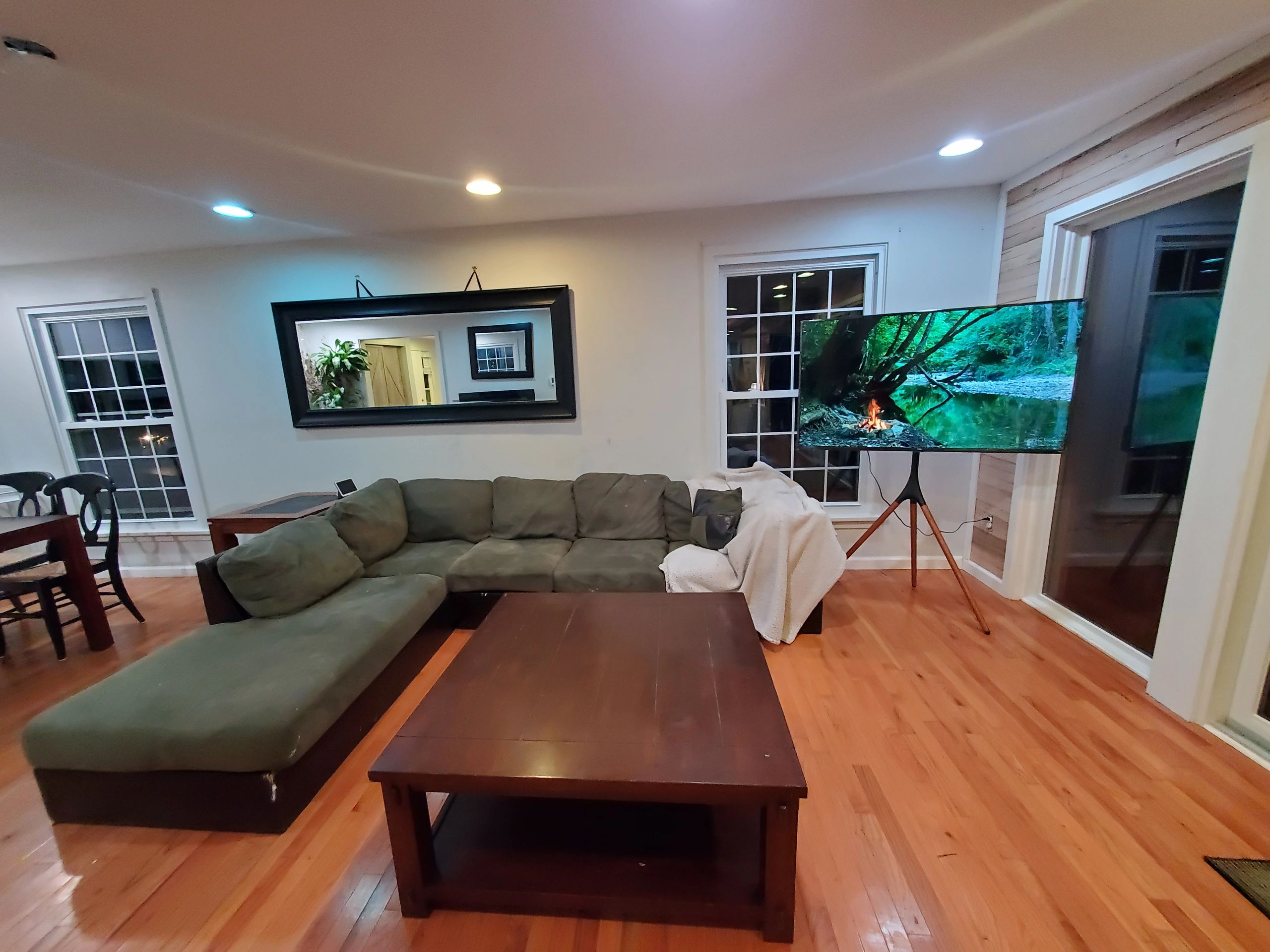 Cozy living room with green sectional sofa and TV on tripod stand.