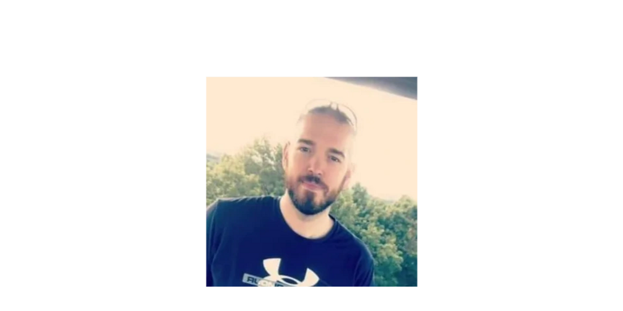 Man with beard wearing a black Under Armour shirt outdoors.