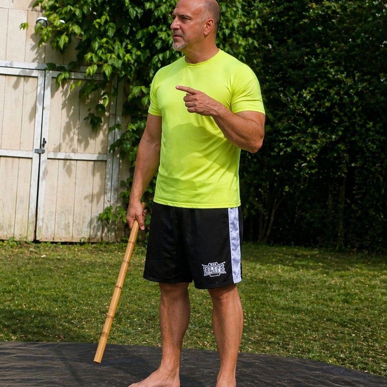 Man in yellow shirt holding a wooden stick outdoors.