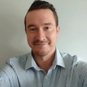Smiling man in checkered shirt taking a selfie.