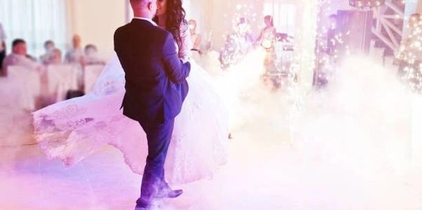 Bride and groom dancing to music at a wedding with a background of sparklers and fog machine clouds