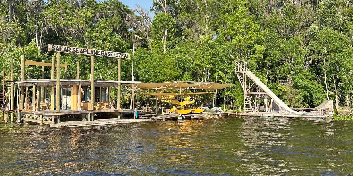 Seaplane base with a yellow seaplane docked by the water and a wooden ramp.