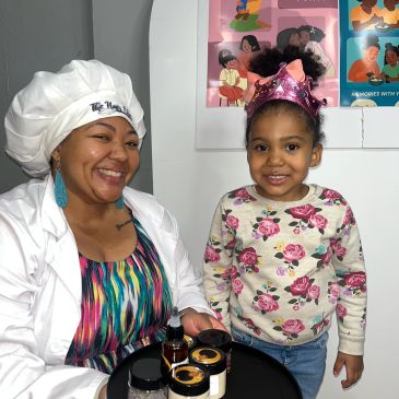 Smiling woman in chef hat with young girl wearing a pink crown.