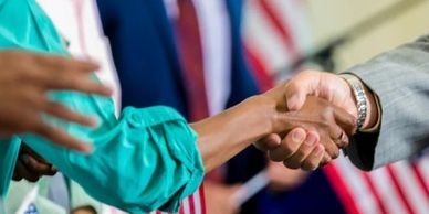 People shaking hands with American flags in the background.