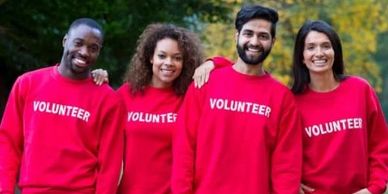 Group of diverse volunteers in red sweatshirts smiling outdoors.