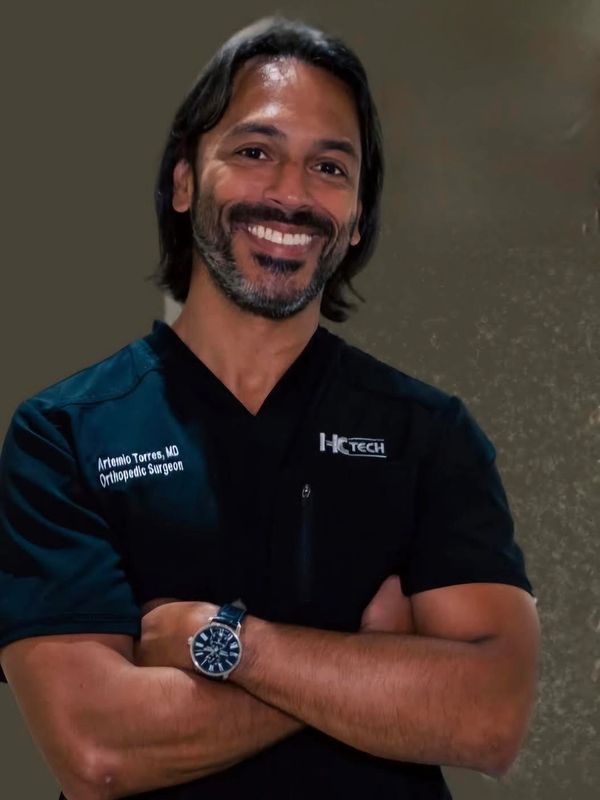 Smiling orthopedic surgeon with crossed arms in medical scrubs.