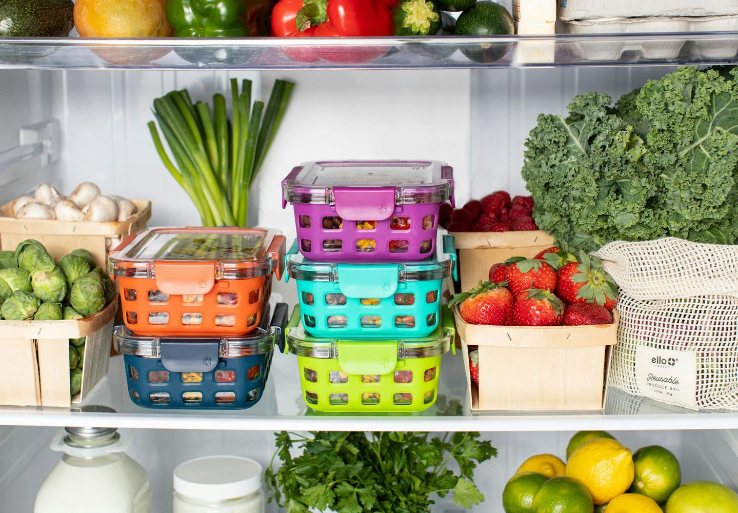 Colorful food storage containers with fresh fruits and vegetables in a refrigerator.