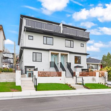 Modern duplex home with white siding and black trim under a bright blue sky.