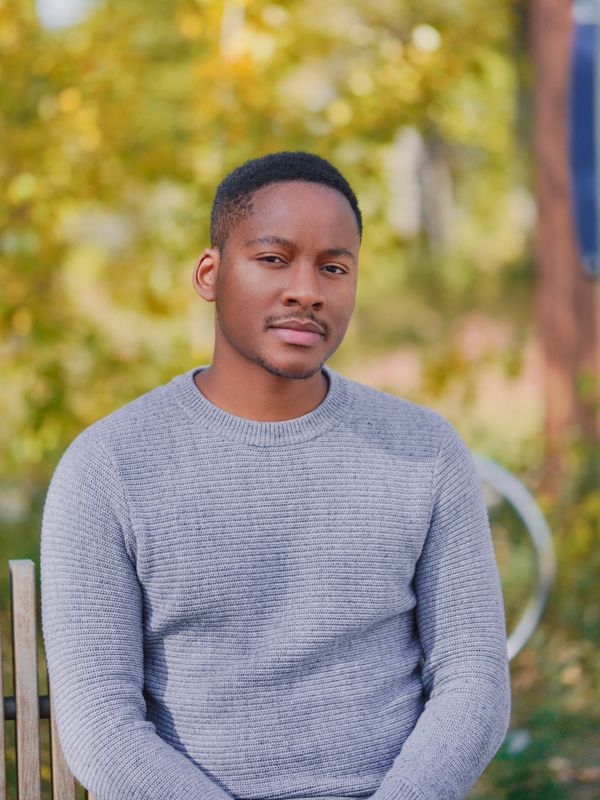 Man in a gray sweater sitting outdoors with a calm expression.
