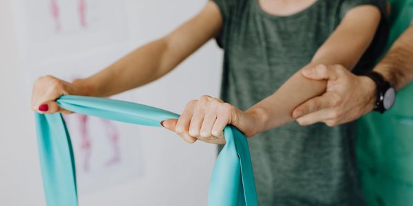 Man standing behind woman, helping her with rehabilitation exercises with a gren band