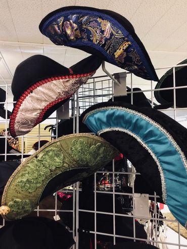 Ornate, colorful hats with floral and decorative patterns displayed on white racks.