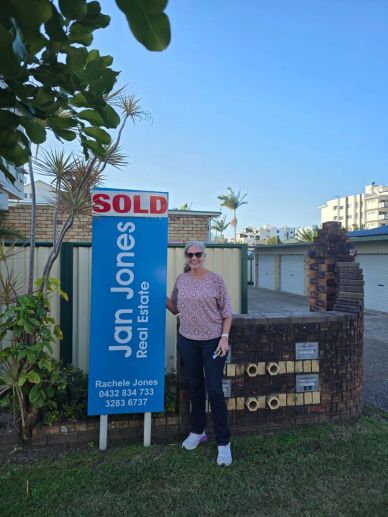 Woman standing next to a sold real estate sign.